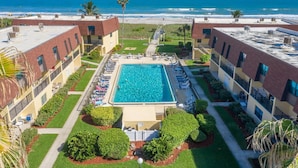 Una piscina en la azotea con vistas a la playa, rodeada de edificios con balcones y un jardín cuidado.