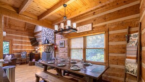 A wooden cabin interior with a dining table set for four, a fireplace, and a stone wall. - 4-Bed/Bath Cabin: Hot Tub, Game Room, Pet-Friendly! (Seven Devils)