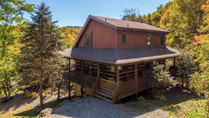 A wooden cabin with a covered deck and a small porch, surrounded by trees and a clear sky. - 4-Bed/Bath Cabin: Hot Tub, Game Room, Pet-Friendly! (Seven Devils)
