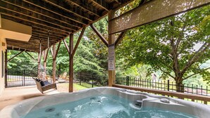 A hot tub area with a wooden deck, a swing chair, and a fenced garden view. - 4-Bed/Bath Cabin: Hot Tub, Game Room, Pet-Friendly! (Seven Devils)