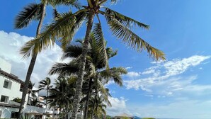 A wooden boardwalk along a beach with palm trees and beach umbrellas. - Apartamento Arenas del Edén, Same Club Casablanca (Tonchigüe)