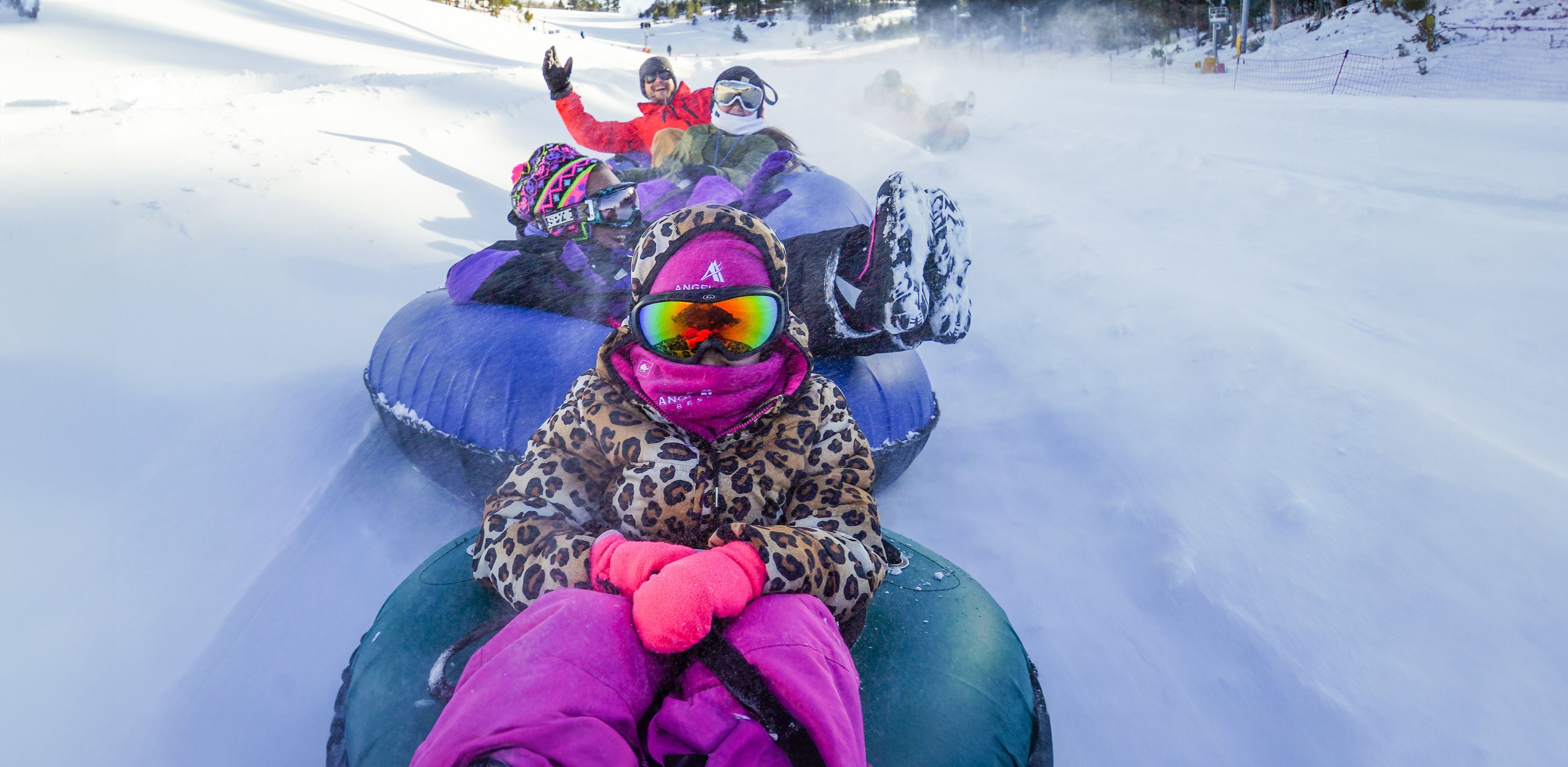 Una persona con chaqueta de leopardo y guantes rosas sentada en un flotador inflable para nieve.