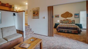 A room with a sofa, a wooden coffee table, a patterned bedspread, and a staircase leading to another level.