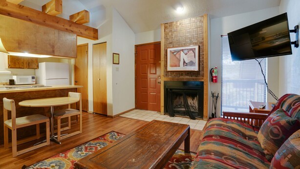A cozy living room with a fireplace, wooden furniture, and a flat-screen TV mounted on the wall. - Condo close to the Chile Express (Angel Fire)