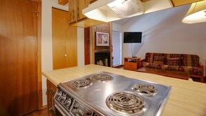 A compact kitchen with a stove, wooden cabinets, and a small dining area with a sofa. - Condo close to the Chile Express (Angel Fire)