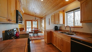 A kitchen with wooden cabinets, a stove, and a dining area with chairs and a table. - Townhome with 1st Hole Golf Course Views (Angel Fire)