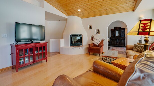 A living room with a wooden ceiling, a television, a fireplace, a red cabinet, and a sofa. - Townhome with 1st Hole Golf Course Views (Angel Fire)