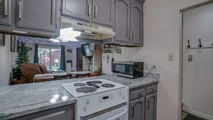 A kitchen with granite countertops, a white stove, and a microwave. There is a dining area with a table and chairs, and a Christmas tree. - Comfy Condo near Shuttle Pick up (Angel Fire)