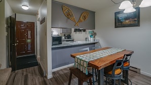 A kitchen with a wooden table and chairs, a gray backsplash, and a hanging light fixture. - Comfy Condo near Shuttle Pick up (Angel Fire)
