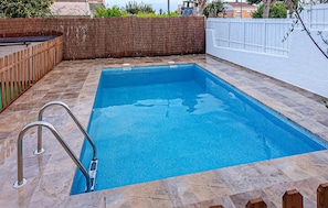 Una piscina rectangular con superficie de agua azul cristalina, rodeada de baldosas de piedra y una valla de madera.