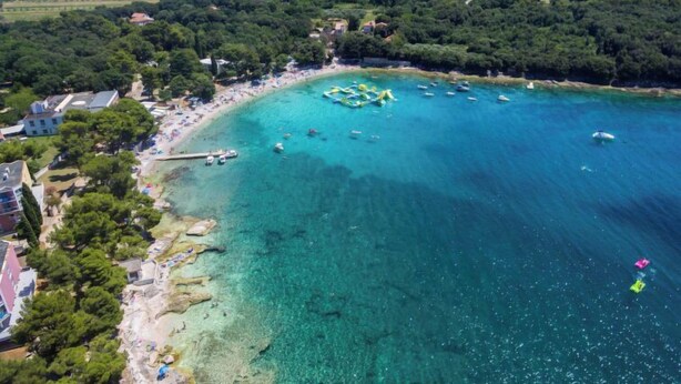 Vue aérienne d’une zone côtière avec des eaux turquoise limpides, une plage de sable et un petit quai.