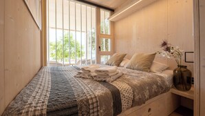 A bedroom with a large window, a bed with a quilt, a bedside table with a vase, and wooden walls. - Vanellus Villas Sleeps 6 With Jacuzzi (Pakostane)