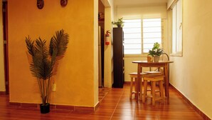 A hallway with wooden flooring, a potted plant, a small table with chairs, and a window with blinds. - Loft in Roma Sur: King Size Bed (Cuauhtémoc)