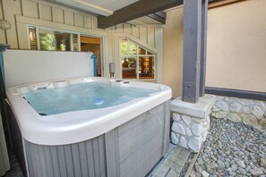 A hot tub in a covered outdoor area with a stone wall and wooden deck. - Village Gem: 2BR, 2BA, Private H/T, Free Parking, Heart of the Village, Free Bus (Whistler)