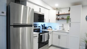 A modern kitchen with stainless steel appliances, white cabinetry, and a tiled backsplash. - Cozy 1 bedroom suite-apartment. (Port Richey)