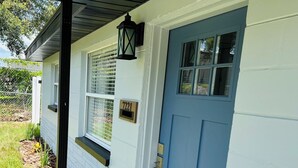 A house with a blue front door, a window with a number plate, and a black lantern on the wall. - Cozy 1 bedroom suite-apartment. (Port Richey)
