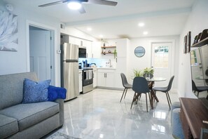 A modern kitchen with stainless steel appliances, a dining area with a round table and chairs, and a living room with a sofa and a blue pillow. - Cozy 1 bedroom suite-apartment. (Port Richey)