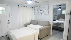 A bedroom with a bed, a sofa, a ceiling fan, a door, and a painting on the wall. - Cozy 1 bedroom suite-apartment. (Port Richey)