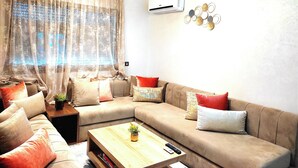A living room with a sectional sofa, a coffee table, and a wall-mounted air conditioner.