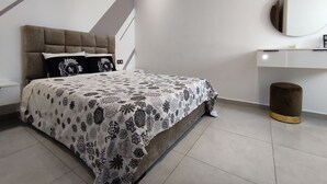 A modern bedroom with a tufted headboard, a patterned bedspread, a bedside table, a mirror, and a small stool.
