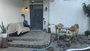 Patio con suelo de piedra, una cama, sillas y plantas en macetas.