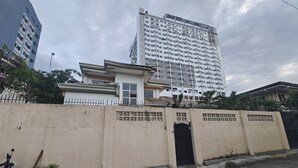 Un edificio residencial con entrada protegida por un portón, un pequeño porche y un rascacielos alto contiguo.