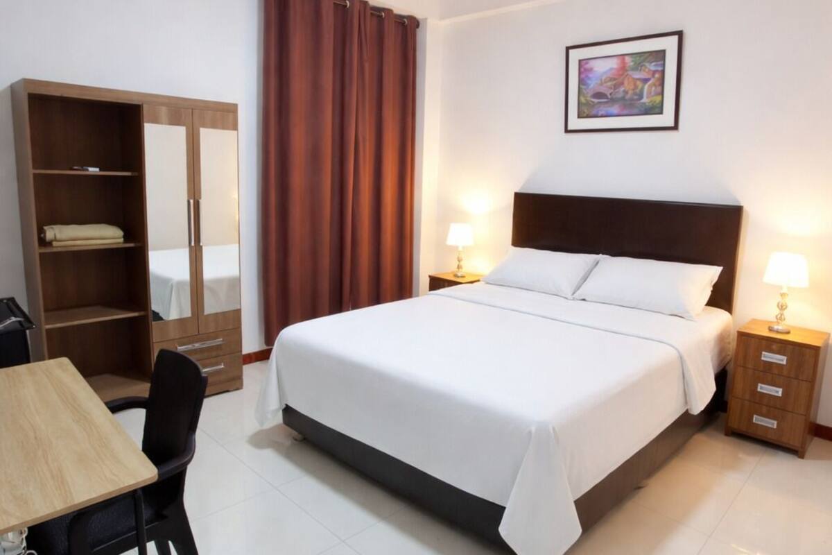 Ein Hotelzimmer mit Bett, Schreibtisch, Kleiderschrank und Nachttisch mit Lampen.