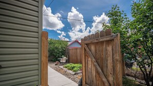 A wooden gate leading to a backyard with a red-roofed shed, a concrete pathway, and various plants. - First Street Flat in Downtown Moscow (Moscow)