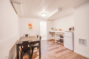 A compact kitchen with white appliances, a dining area with a wooden table and chairs, and a door leading to another room. - First Street Flat in Downtown Moscow (Moscow)