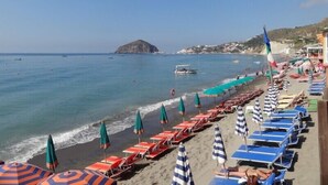 A beach with rows of sun loungers and umbrellas, a clear sky, and a distant island. - Villa La Favola Suite Ischia Terrace with view (Barano D'ischia)