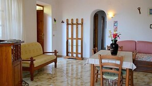 A living room with a wooden sofa, a dining table with chairs, a wooden cabinet, and a door leading to another room. - Villa La Favola Suite Ischia Terrace with view (Barano D'ischia)