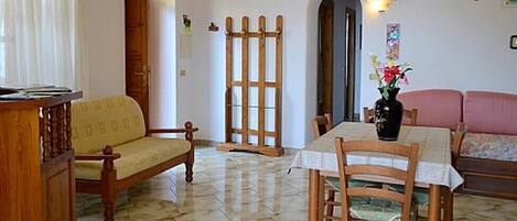A living room with a wooden sofa, a dining table with chairs, a wooden cabinet, and a door leading to another room.