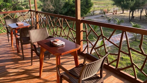 Terraza de madera con mobiliario exterior, vista a la playa y jardín cercado.