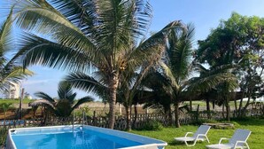 Una piscina rectangular con estructura blanca, rodeada de palmeras y una valla de madera.
