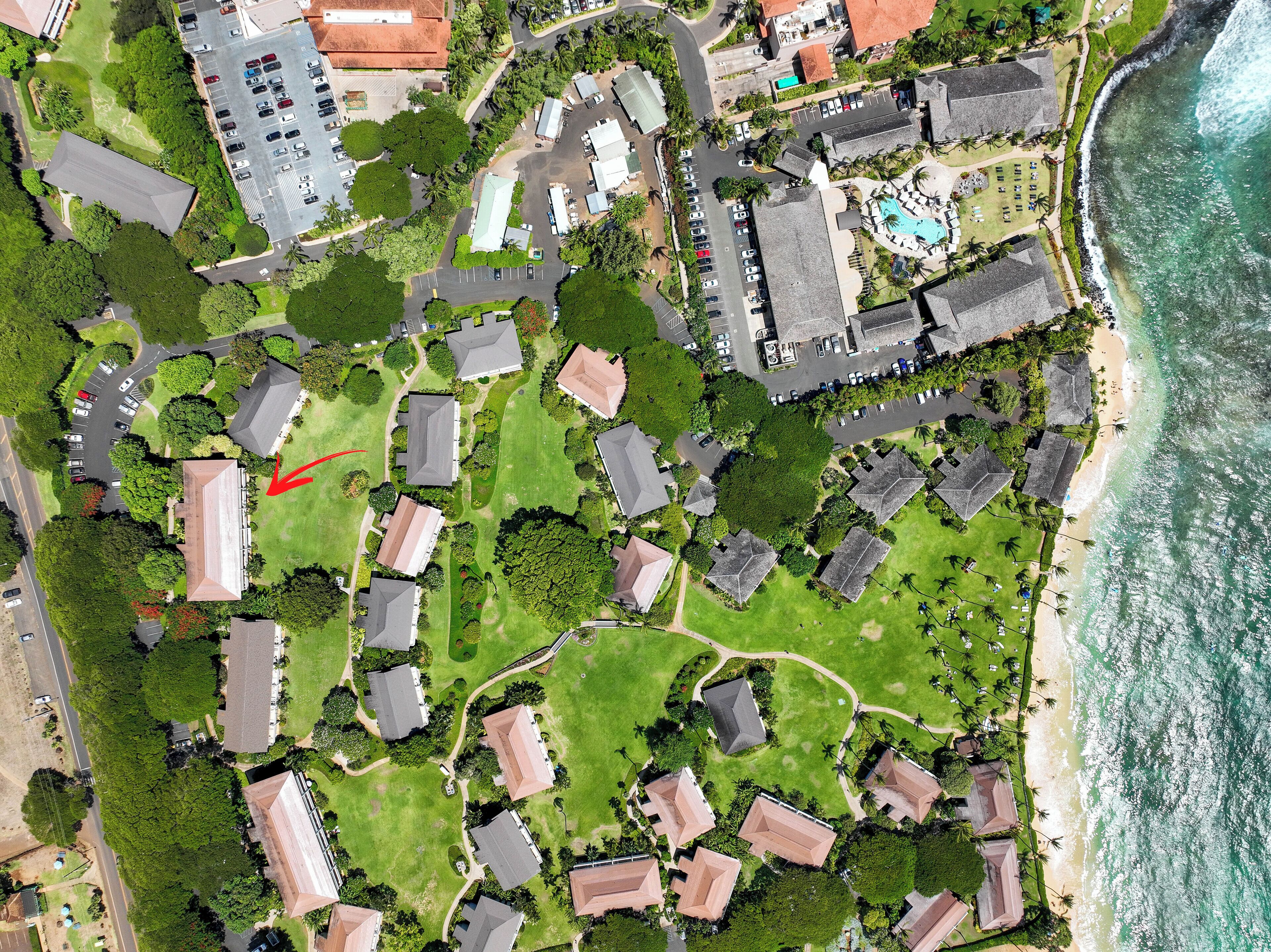 Vue aérienne d’une station balnéaire comprenant plusieurs bâtiments de style bungalow, un espace piscine central et une plage.