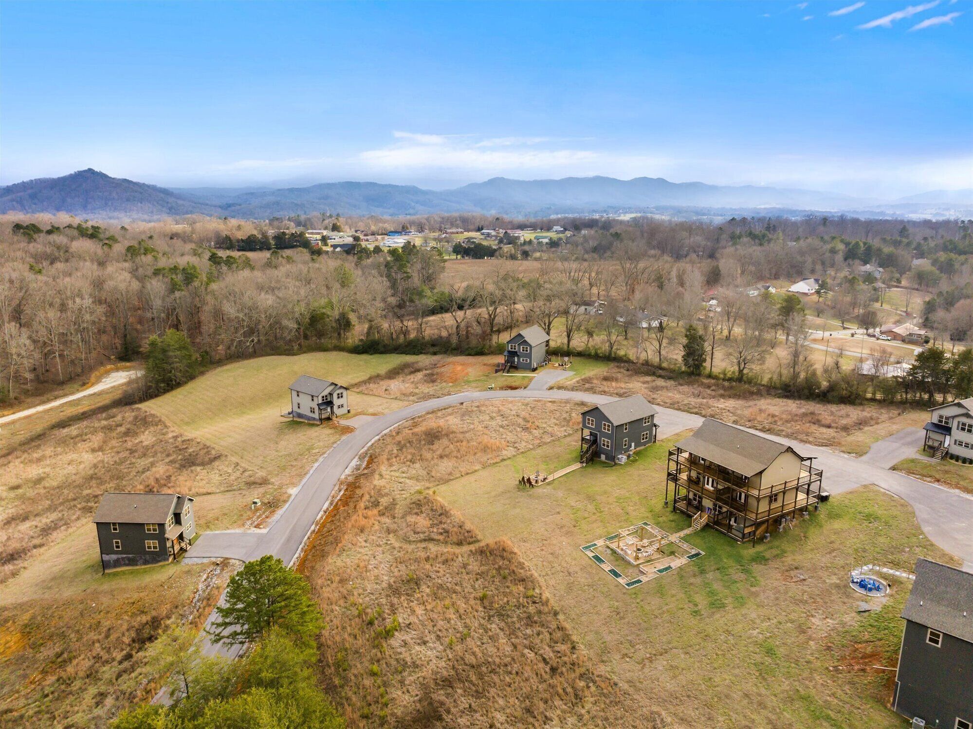 A rural landscape with several houses, a winding road, and a large building with a wooden deck.