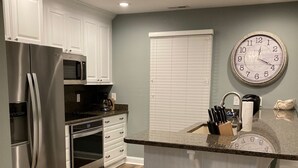 A modern kitchen with white cabinetry, stainless steel appliances, a wooden floor, and a large wall clock. - BEAUTIFULLY DECORATED ~ CLOSE TO THE BEACH ~ 5 BEDROOM/4 BATH  (Corolla)
