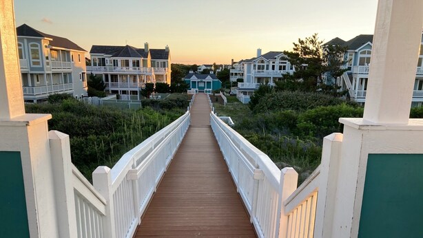 A wooden boardwalk leading to a row of houses with white railings and green accents. - BEAUTIFULLY DECORATED ~ CLOSE TO THE BEACH ~ 5 BEDROOM/4 BATH  (Corolla)