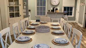 A dining room with a long table set for six, surrounded by white chairs. - BEAUTIFULLY DECORATED ~ CLOSE TO THE BEACH ~ 5 BEDROOM/4 BATH  (Corolla)