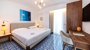 A hotel room with a large bed, a desk, and a chair. There is a painting on the wall and a window with curtains. - PRESTIGE SEA VIEW VILLA SCANNELLA (Forio)