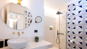 A modern bathroom with a large round mirror, a white sink, and a shower with geometric tile walls. - PRESTIGE SEA VIEW VILLA SCANNELLA (Forio)