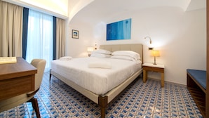 Une chambre d’hôtel avec un lit, un bureau, une chaise, une table de chevet avec une lampe et un tableau au mur.
