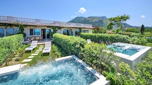 Un espace piscine doté de deux bains à remous et de chaises longues, entouré d’une végétation luxuriante et avec une chaîne de montagnes en toile de fond.