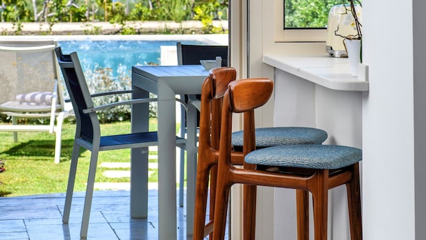 Une terrasse avec une table et deux chaises en bois, donnant sur une piscine et l’océan.