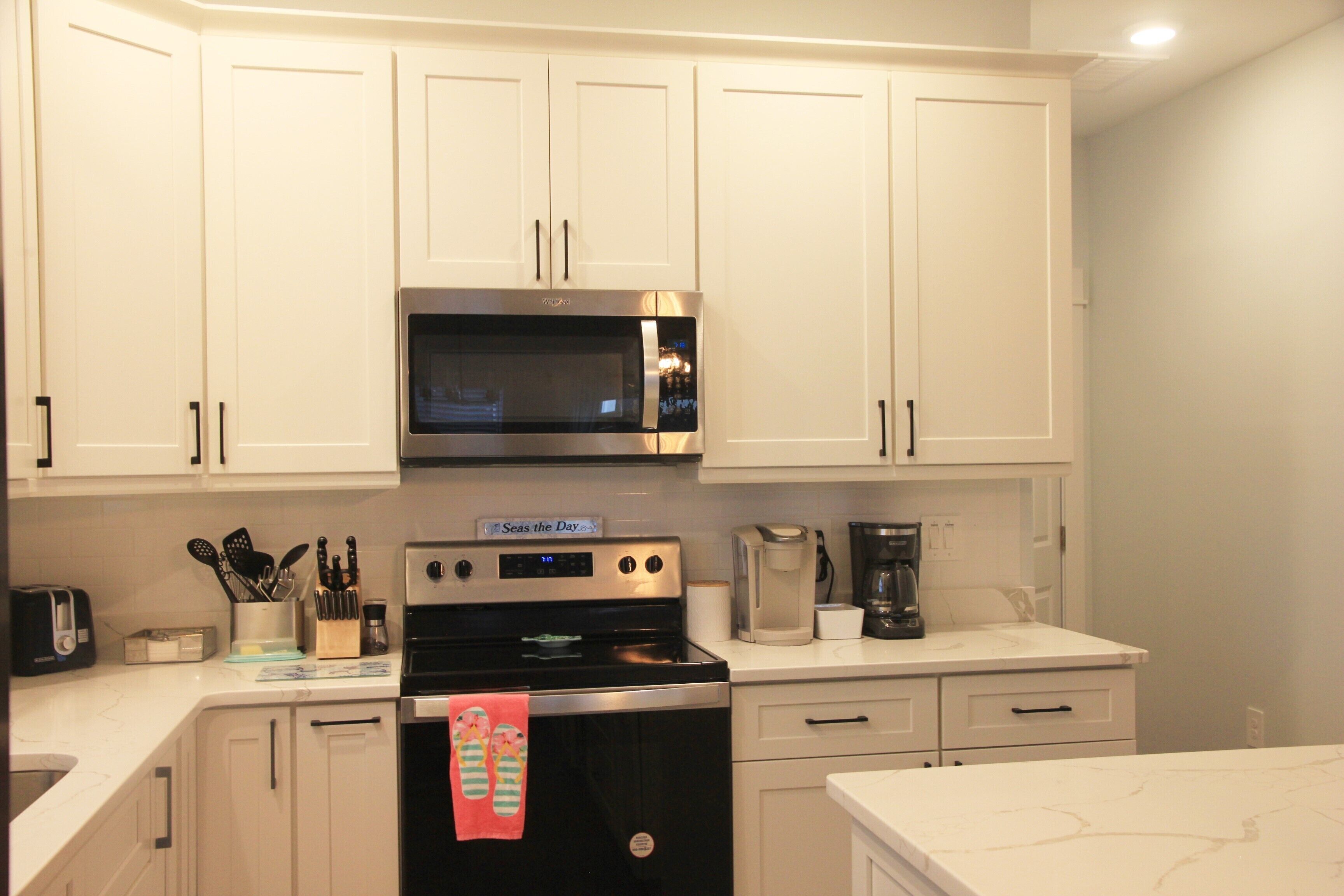 A kitchen with white cabinets, a microwave, a stove, and a coffee maker.
