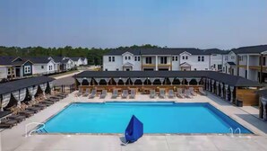 A swimming pool with lounge chairs and umbrellas, surrounded by a row of houses with a covered walkway. - "Seas the Day", located in the heart of beautiful Corolla, Outer Banks of NC (Corolla)