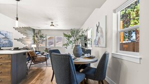 A modern kitchen with a central island, wooden flooring, and a dining area with blue upholstered chairs. - Brand New Dog-Friendly Getaway! Perfectly Positioned for Boise Adventures! Walk to Grocery & More! (Boise)