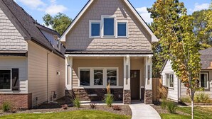 A two-story house with a gabled roof, a front porch with a stone foundation, and a well-maintained lawn. - Brand New Dog-Friendly Getaway! Perfectly Positioned for Boise Adventures! Walk to Grocery & More! (Boise)