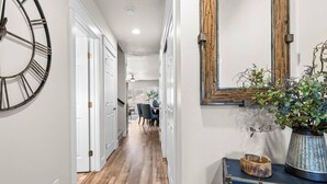 A hallway with a wooden floor, a clock, a mirror, and a plant on a dresser. - Brand New Dog-Friendly Getaway! Perfectly Positioned for Boise Adventures! Walk to Grocery & More! (Boise)
