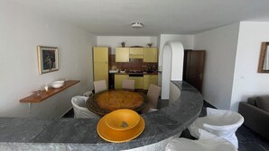 Een moderne woonkamer met een gebogen marmeren aanrecht, een ronde eettafel en een keuken met gele kastjes en een witte spoelbak.